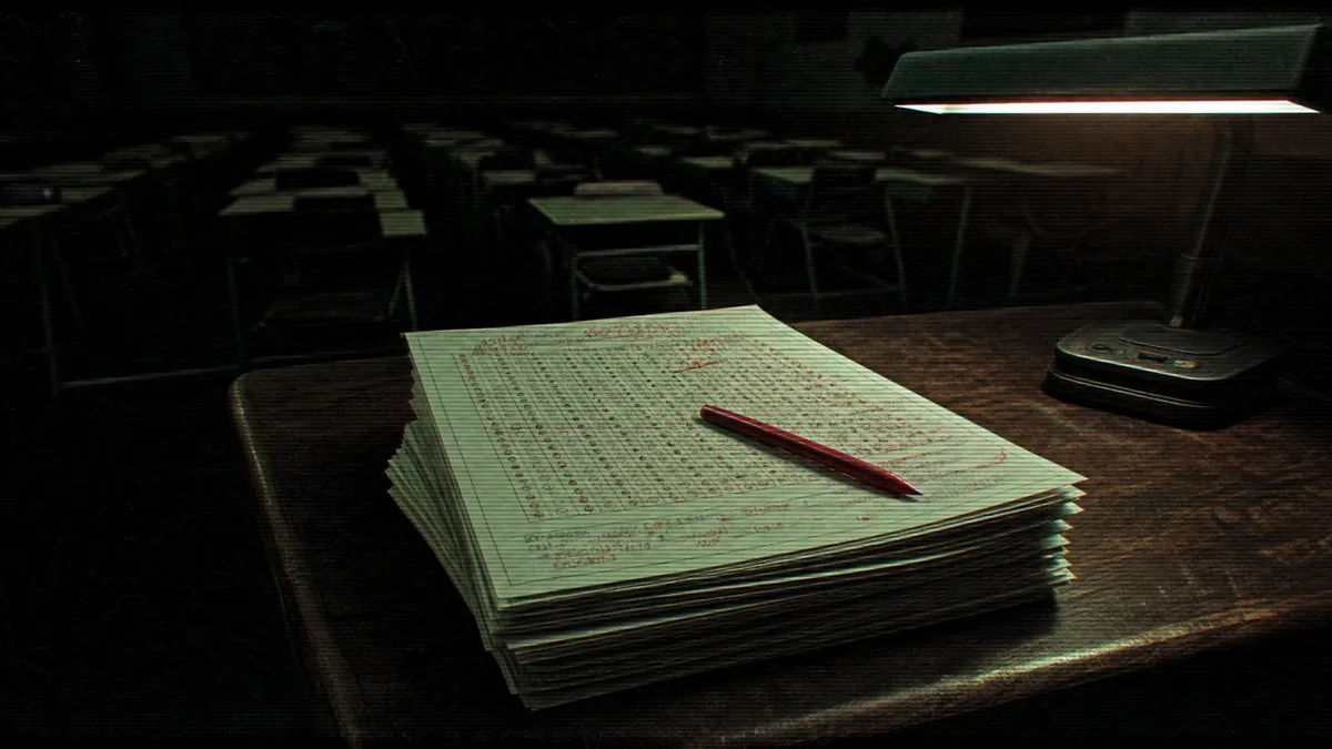 A stack of marked exam papers and a red pencil under a desk lamp